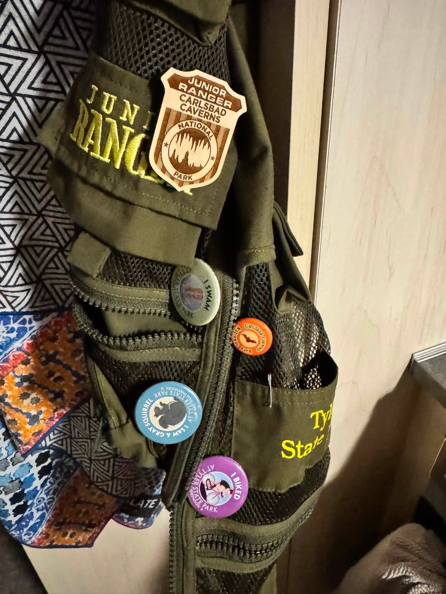 A Junior Ranger vest hanging in the Airstream, with the wooden Carlsbad Caverns Junior Ranger badge and a row of park buttons