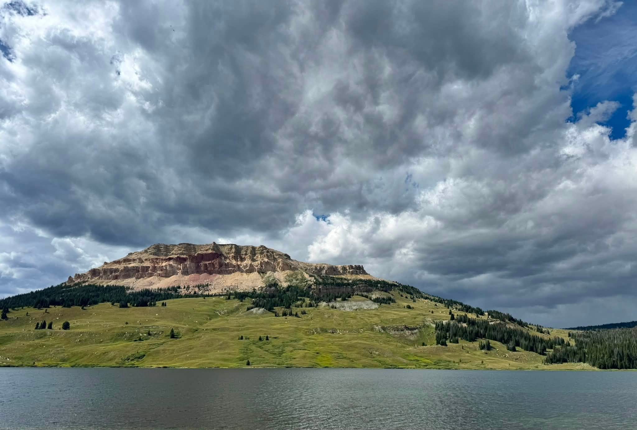 Beartooth Butte rising in bands of red and tan above Beartooth Lake, a towering bank of clouds filling the sky above it