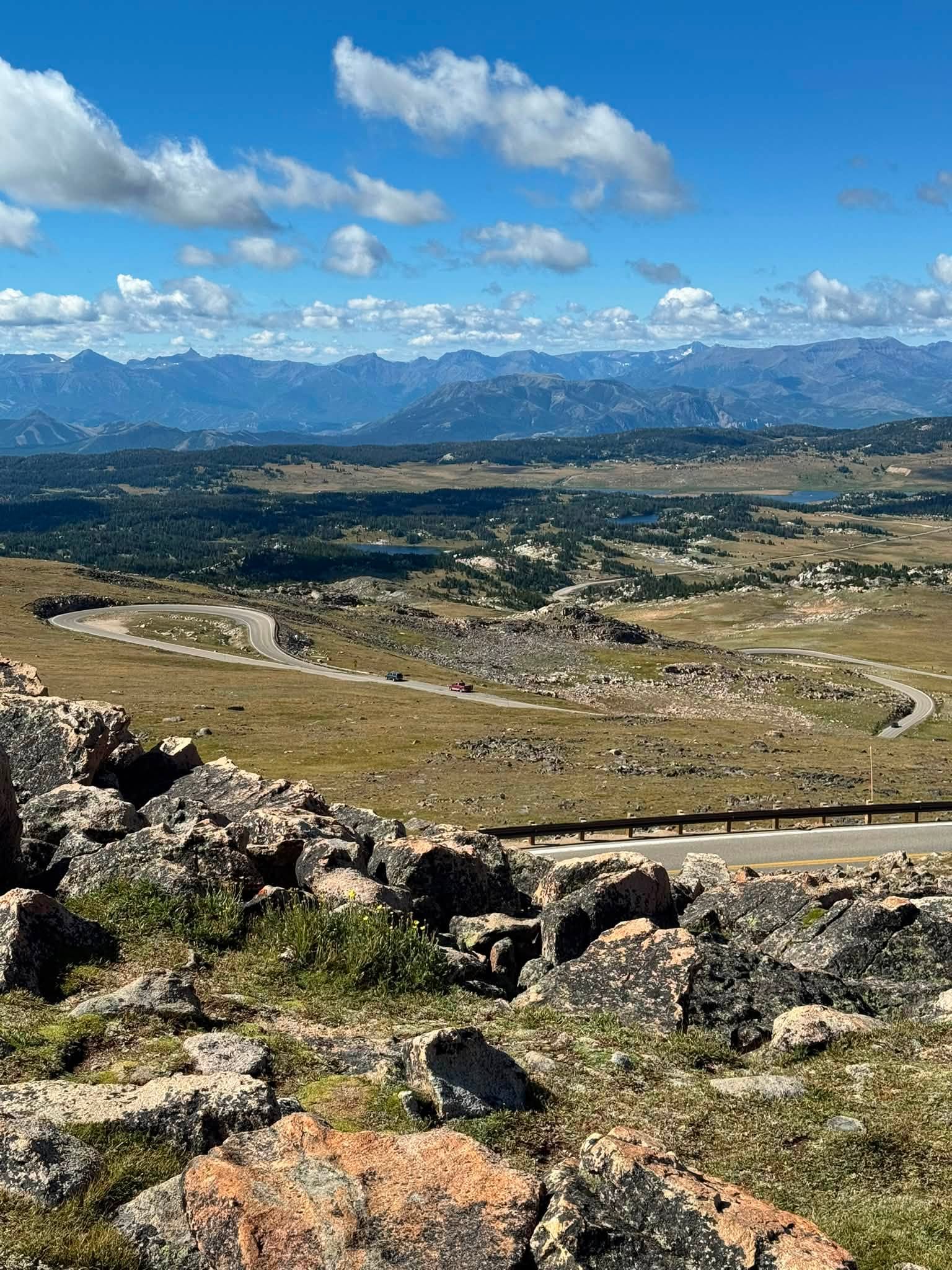 The Beartooth Highway switchbacking across a high open plateau, with lakes scattered below and range after range of mountains fading to the horizon