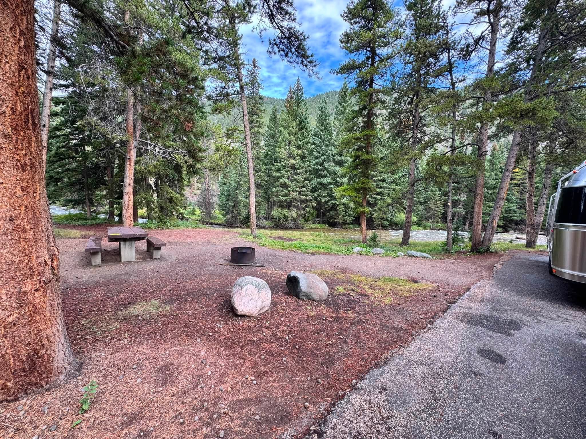 A pine-shaded campsite at Parkside Campground with a picnic table and fire ring, Rock Creek and the forested canyon wall beyond