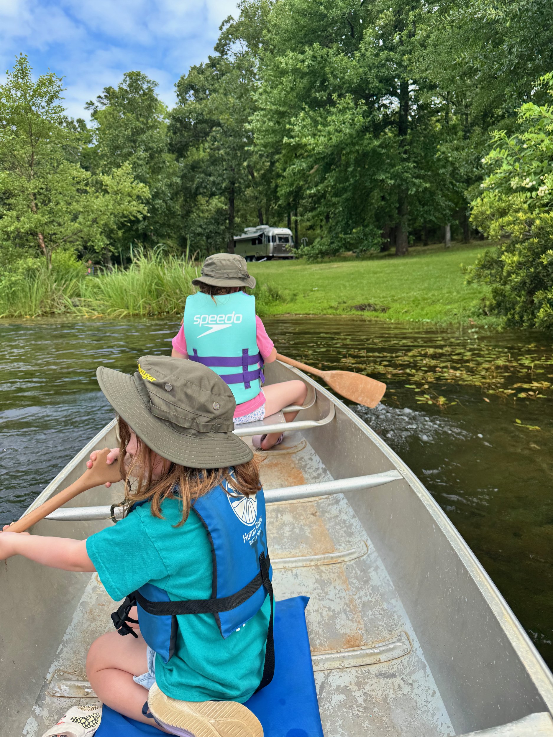 Lillian and Emery paddling a canoe on the lake at Tyler State Park with Belle parked on the shoreline behind them