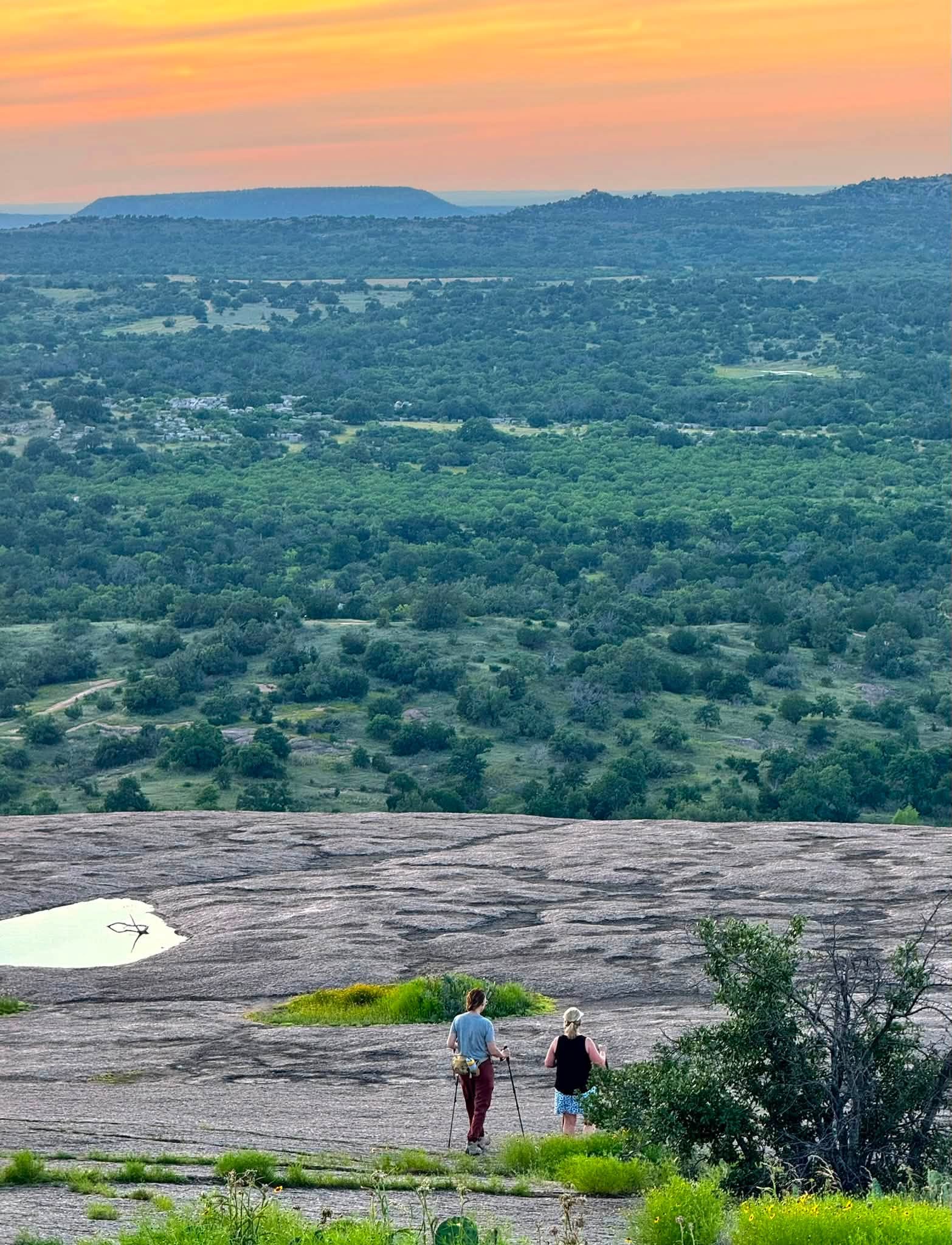 Two hikers on the granite dome at Enchanted Rock, looking out over the Texas Hill Country at sunset