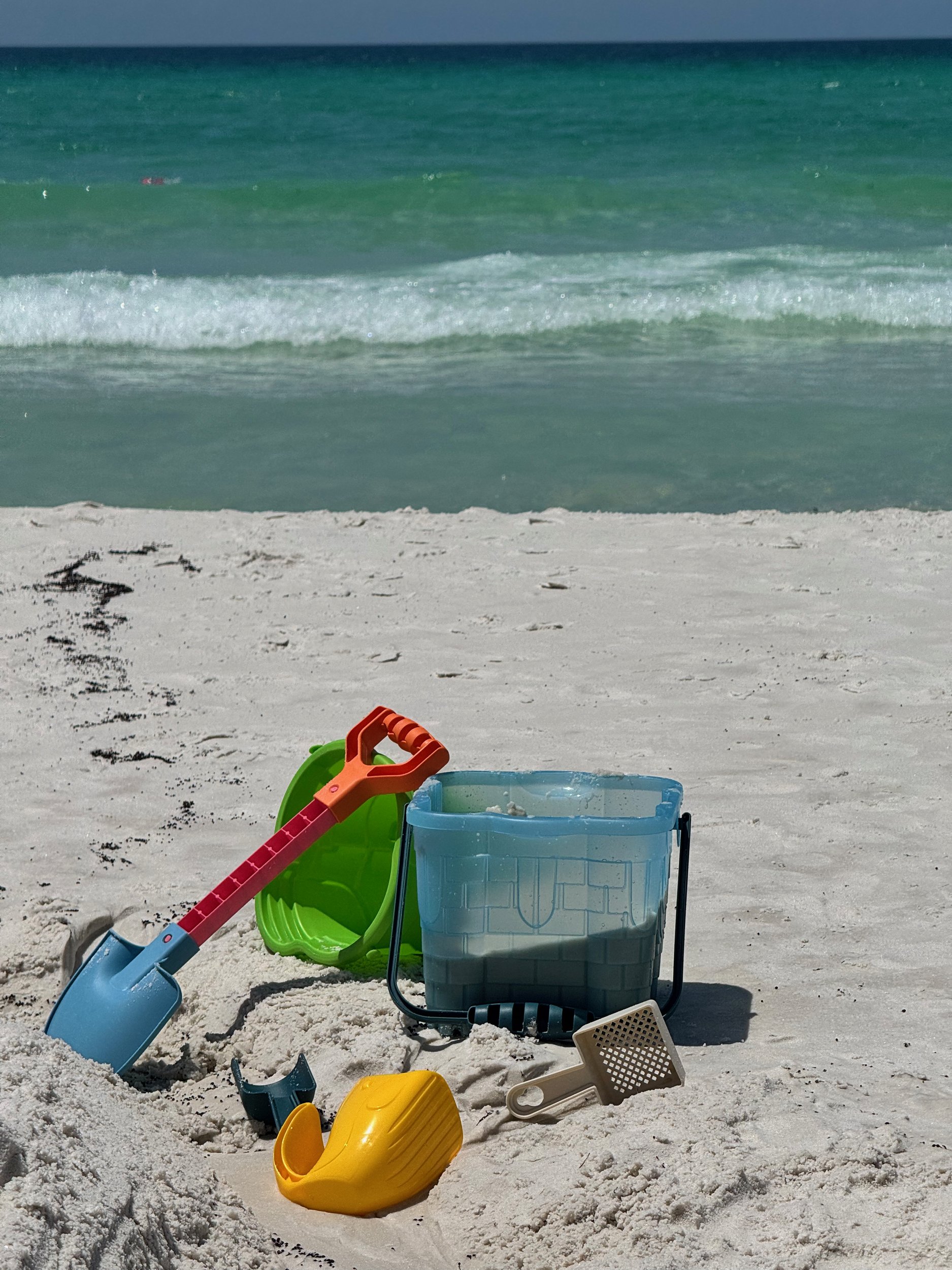 Sand toys on the white sand at WaterColor with the emerald-green Gulf surf behind them